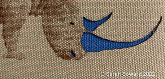 Cropped image of an etched rhino by Sarah Soward. The horns are cut away to show blue fabric underneath.